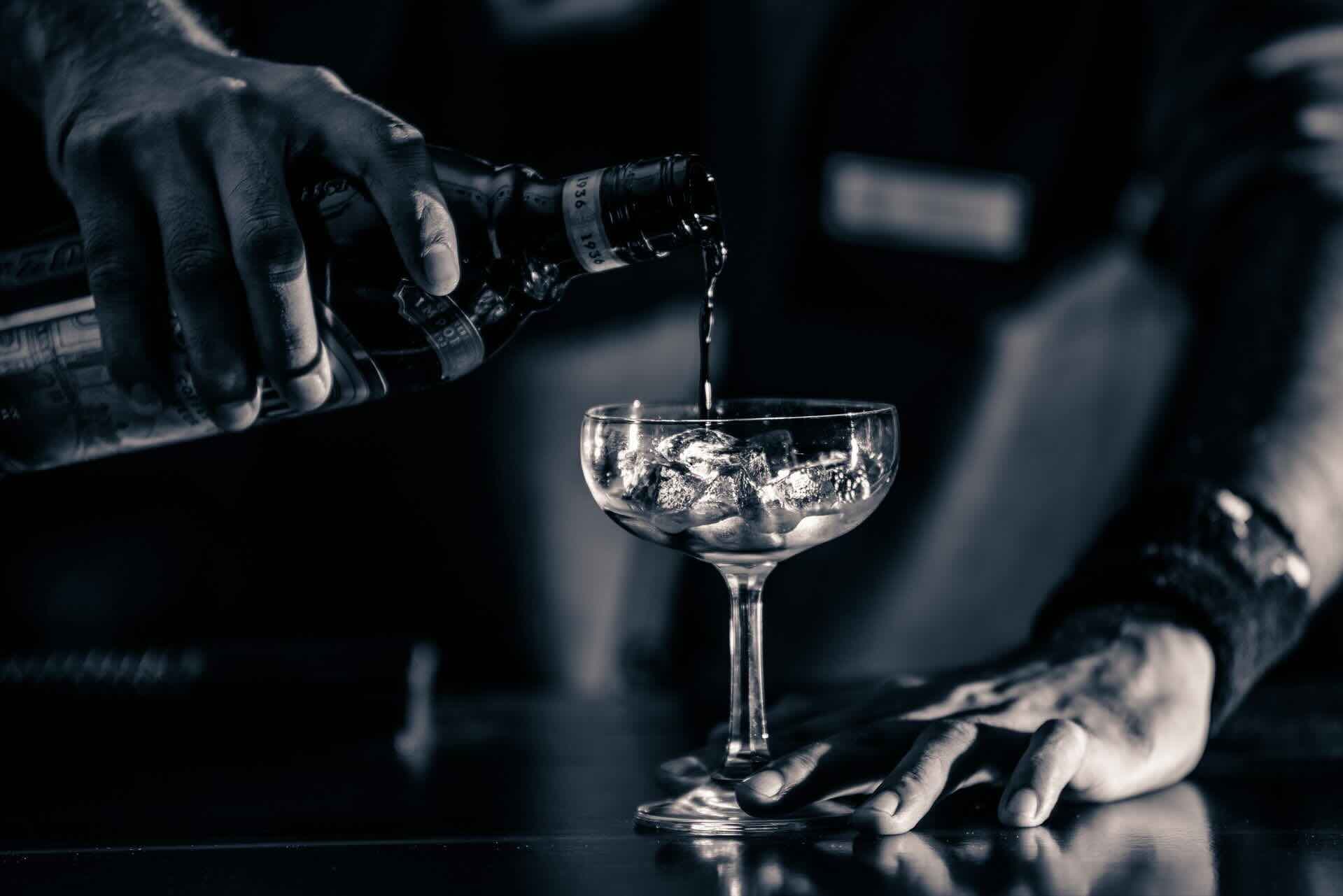 Hands twisting an orange peel over a cocktail at the bar, in low amber light